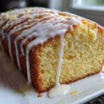 Close-up of a slice of Moist Lemon Loaf covered in thick white lemon glaze and zest.