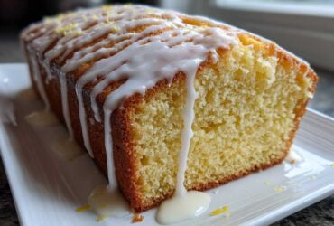 Close-up of a slice of Moist Lemon Loaf covered in thick white lemon glaze and zest.