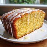 A close-up of a slice of Moist Lemon Loaf with thick white lemon glaze dripping down the sides.