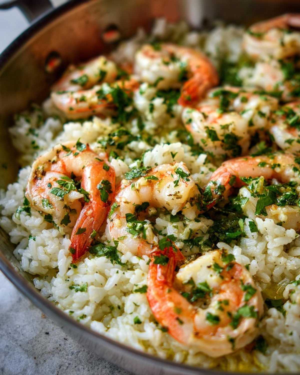 Close-up of cooked shrimp nestled in white rice, topped with garlic and fresh parsley in a one-pan garlic shrimp and rice dish.