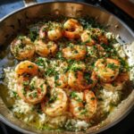 Close-up of cooked shrimp nestled on white rice, seasoned heavily with garlic and parsley in a one-pan garlic shrimp and rice dish.