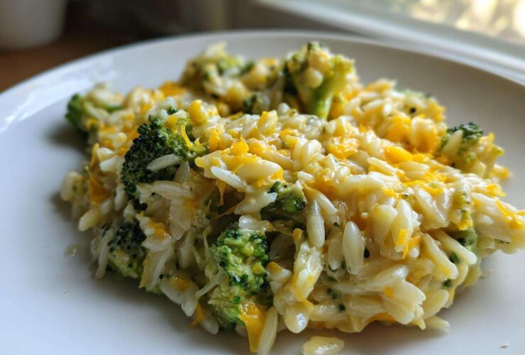 Close-up of a creamy serving of One Pot Broccoli Cheese Orzo topped with melted cheddar cheese.