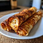 Three crispy, golden brown Oven Rolled Chicken Taquitos showing melted cheese and filling on a white plate.