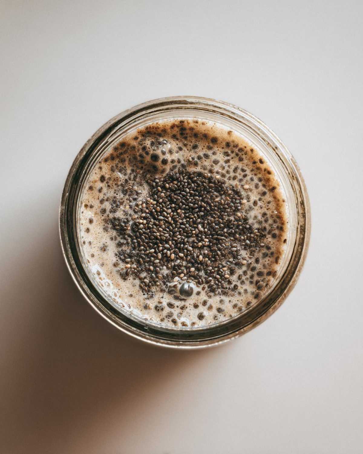 Overhead view of a jar containing freshly made Chia Pudding with visible chia seeds floating on top of the creamy liquid.