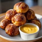 A pile of golden brown, sugar-topped Pretzel Bites served with a small white ramekin of bright yellow beer cheese dip.