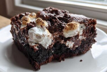 A decadent slice of Rich Marshmallow Chocolate Poke Cake showing gooey chocolate and toasted marshmallows on top.