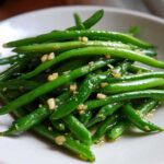 A close-up of vibrant green beans tossed with minced garlic, ready to serve.