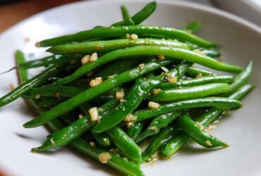 A close-up of vibrant green beans tossed with minced garlic, ready to serve.