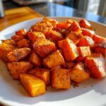 Close-up of perfectly seasoned Roasted Sweet Potatoes cubes, caramelized and sprinkled with herbs, served on a white plate.