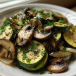 A close-up of freshly Sauteed Zucchini Mushrooms and Onions seasoned with pepper and parsley on a white plate.