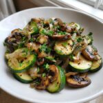 A close-up of perfectly Sauteed Zucchini Mushrooms and Onions, garnished with fresh parsley, served in a white bowl.