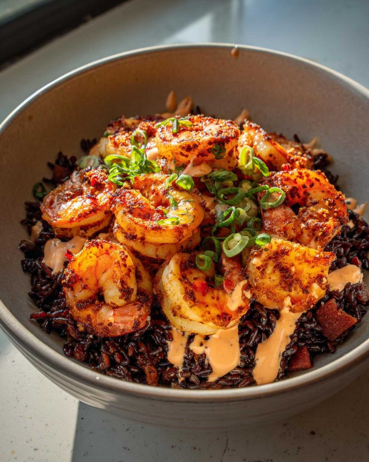 Close-up of a Spicy Cajun Shrimp & Rice Bowl featuring blackened shrimp over dark black rice, drizzled with a creamy sauce and topped with green onions.