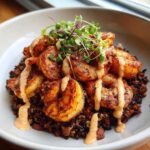 A bowl filled with Spicy Cajun Shrimp & Rice Bowl, featuring blackened shrimp over dark rice, drizzled with a creamy sauce and topped with microgreens.