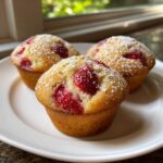 Three golden Strawberry Shortcake Muffins topped with fresh strawberries and dusted with powdered sugar on a white plate.
