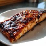 A perfectly cooked fillet of Texas Roadhouse Salmon Copycat with a thick, dark, caramelized glaze on a white plate.