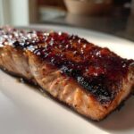 A close-up of a perfectly cooked Texas Roadhouse Salmon Copycat fillet with a dark, shiny glaze on top, resting on a white plate.