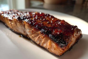 A close-up of a perfectly cooked Texas Roadhouse Salmon Copycat fillet with a dark, shiny glaze on top, resting on a white plate.