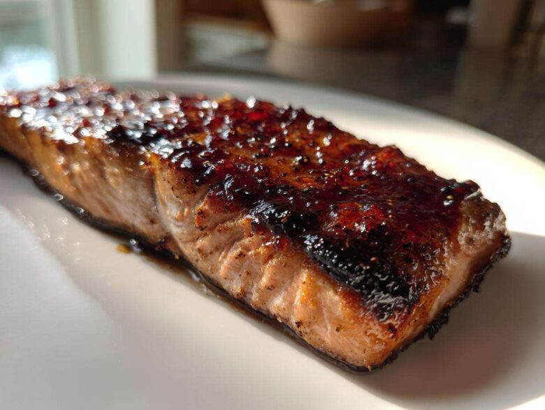 A close-up of a perfectly cooked Texas Roadhouse Salmon Copycat fillet with a dark, shiny glaze on top, resting on a white plate.