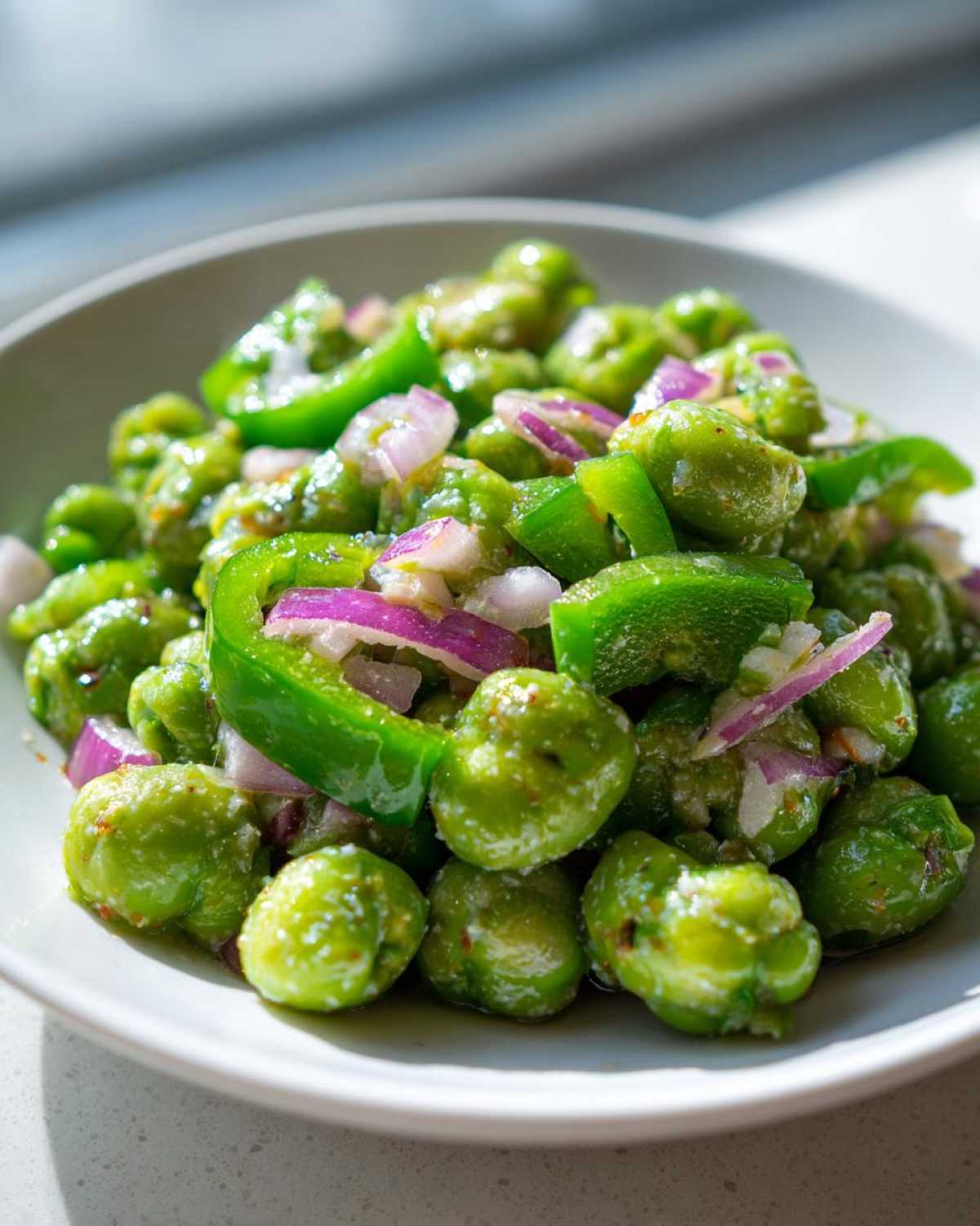 A close-up of a bowl filled with bright green peas, chunks of green bell pepper, and diced red onion in a light dressing, representing Cold Southern Pea Salad.
